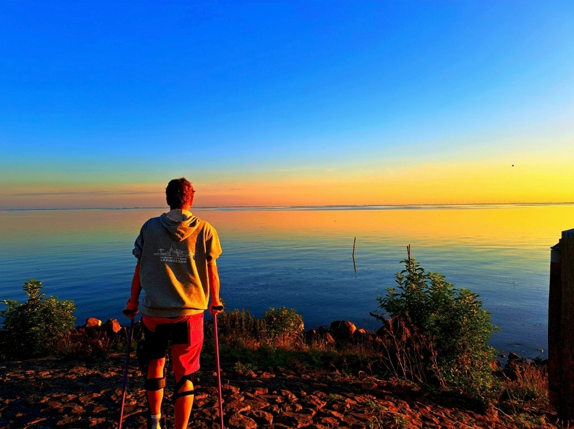Tina Deeken steht mit dem Rücken zum Betrachter vor einem Gewässer, im Hintergrund Sonnenuntergang